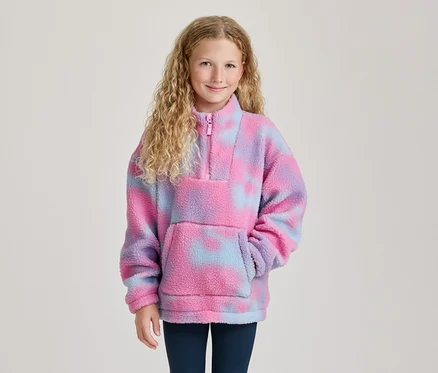 Jeune fille souriante aux cheveux blonds bouclés, portant un pull polaire tie-dye rose, violet et bleu avec un demi-zip et une poche.