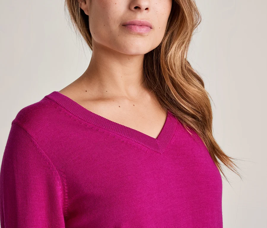 Gros plan d'une femme portant un pull fuchsia à col en V, avec son menton, sa bouche, son nez et ses longs cheveux bruns ondulés visibles.