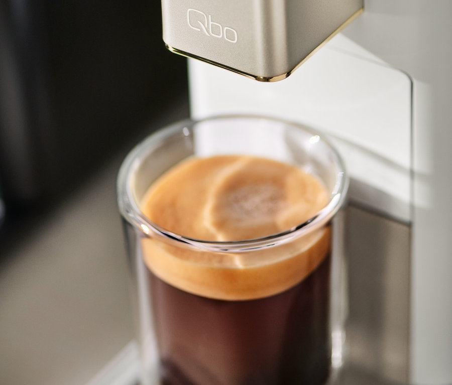 Machine à café Qbo ICONIC Light Gold remplissant un verre de café.
