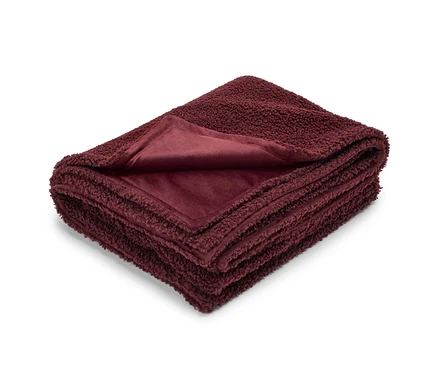 Couverture bordeaux pliée avec une texture en peluche d'un côté et une texture lisse de l'autre.