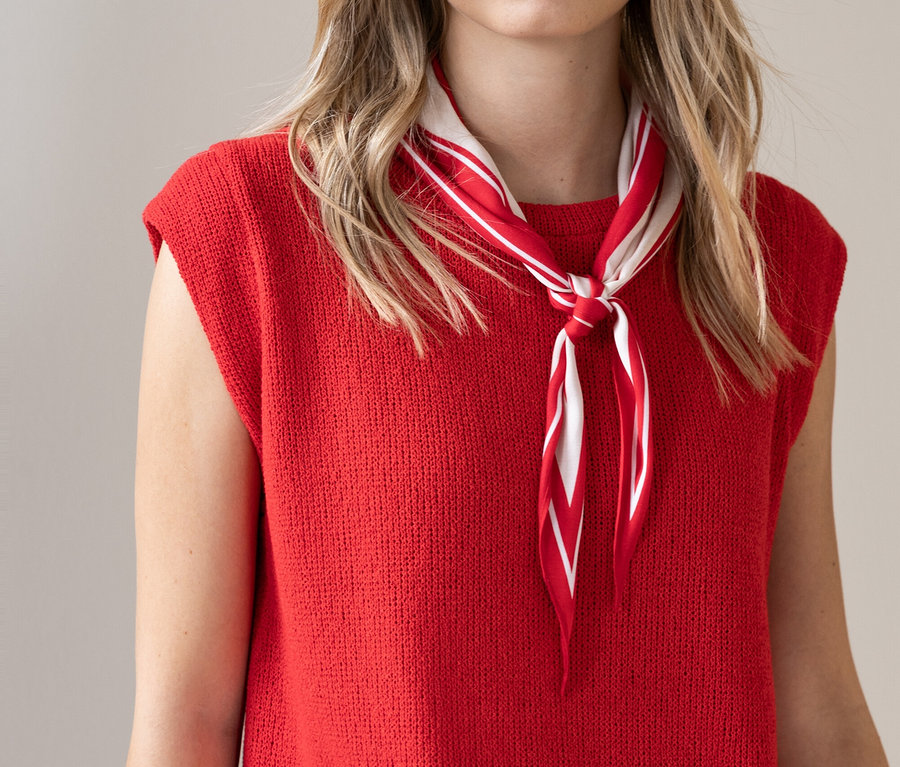 Femme portant un haut en maille rouge et un foulard rayé rouge et blanc.