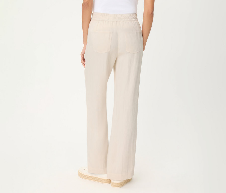 Personne de dos portant un pantalon en lin Olsen beige clair avec taille élastique et poches arrière, et des espadrilles.