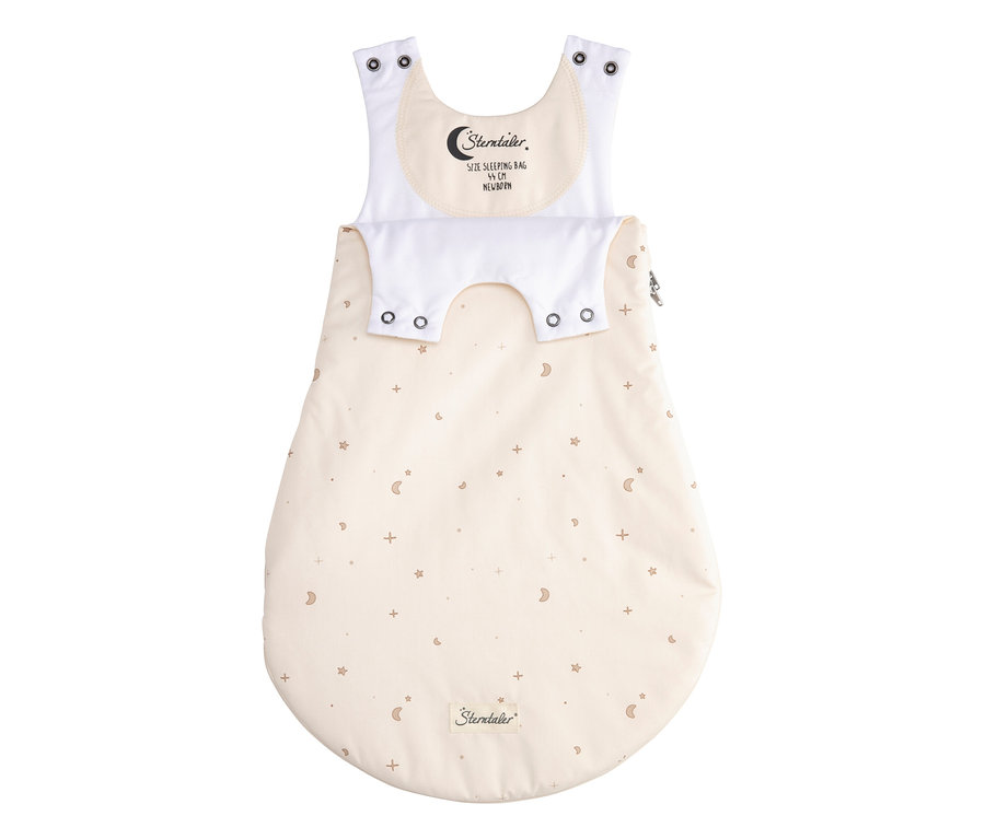 Gigoteuse bébé crème avec un motif d'étoiles, de lunes et de signes plus bruns. Elle présente des bretelles blanches à boutons-pression, un rabat blanc à boutons-pression et une étiquette "Sterntaler, 44 cm Newborn" sur la poitrine. Une fermeture éclair est sur le côté droit.