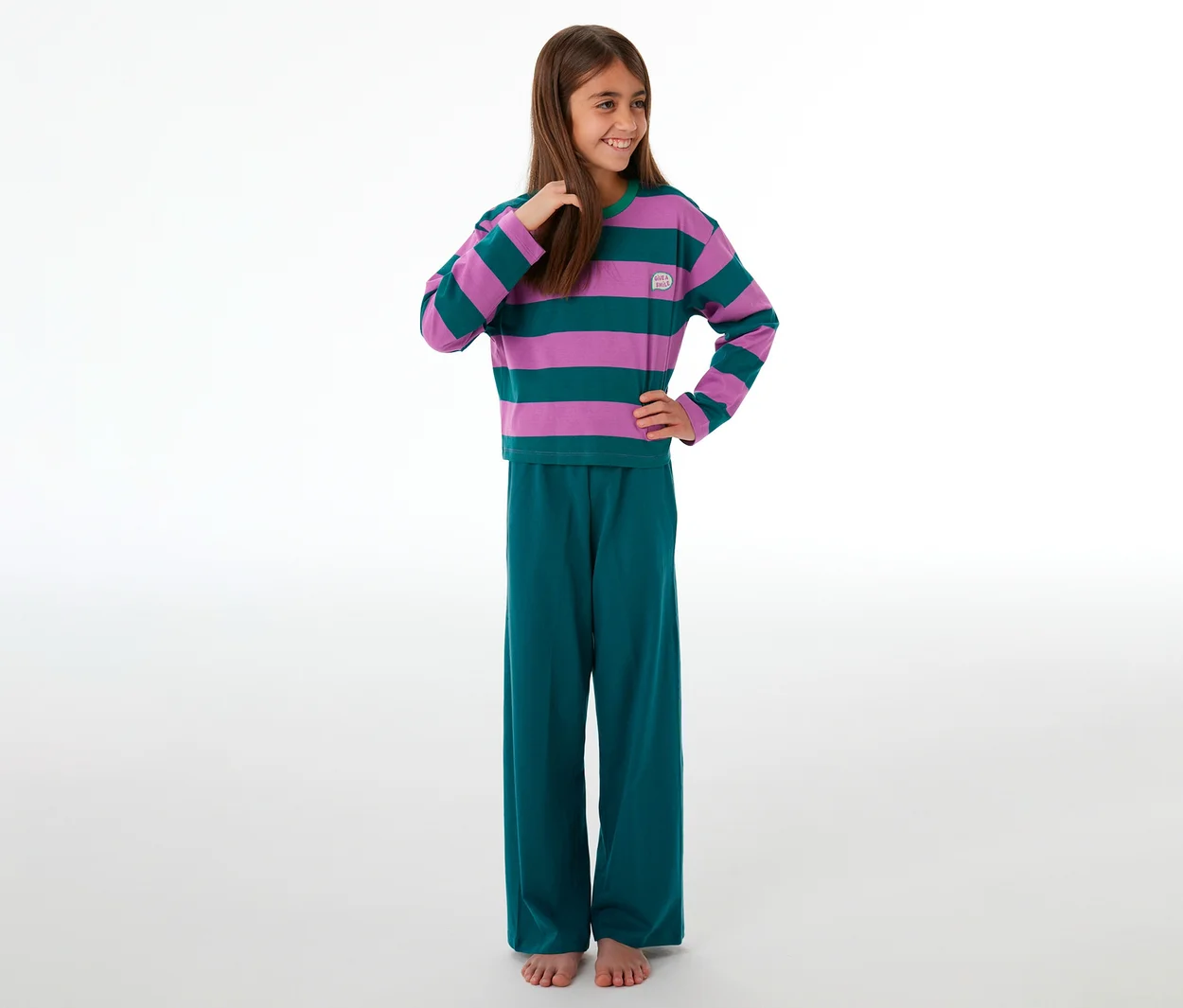 Fille souriante portant un pyjama enfant avec un haut rayé violet et vert et un pantalon vert.
