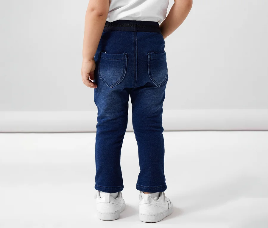 Vue arrière d'un enfant portant un jean en sweat NAME IT et des baskets blanches.