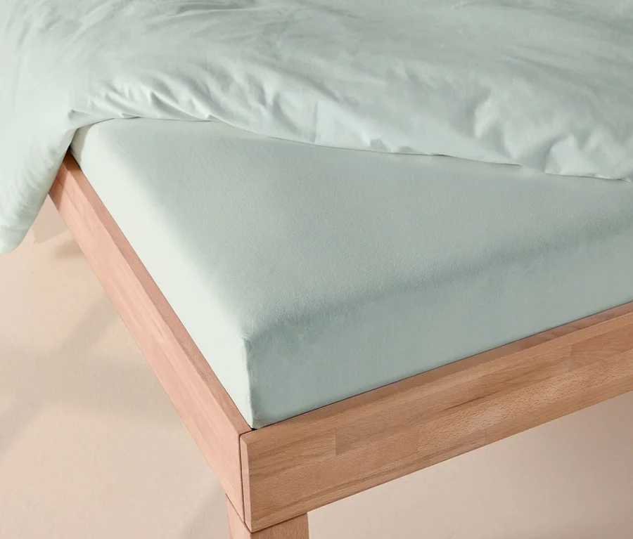 Drap-housse en jersey couleur sauge et couette assortie sur un cadre de lit en bois.