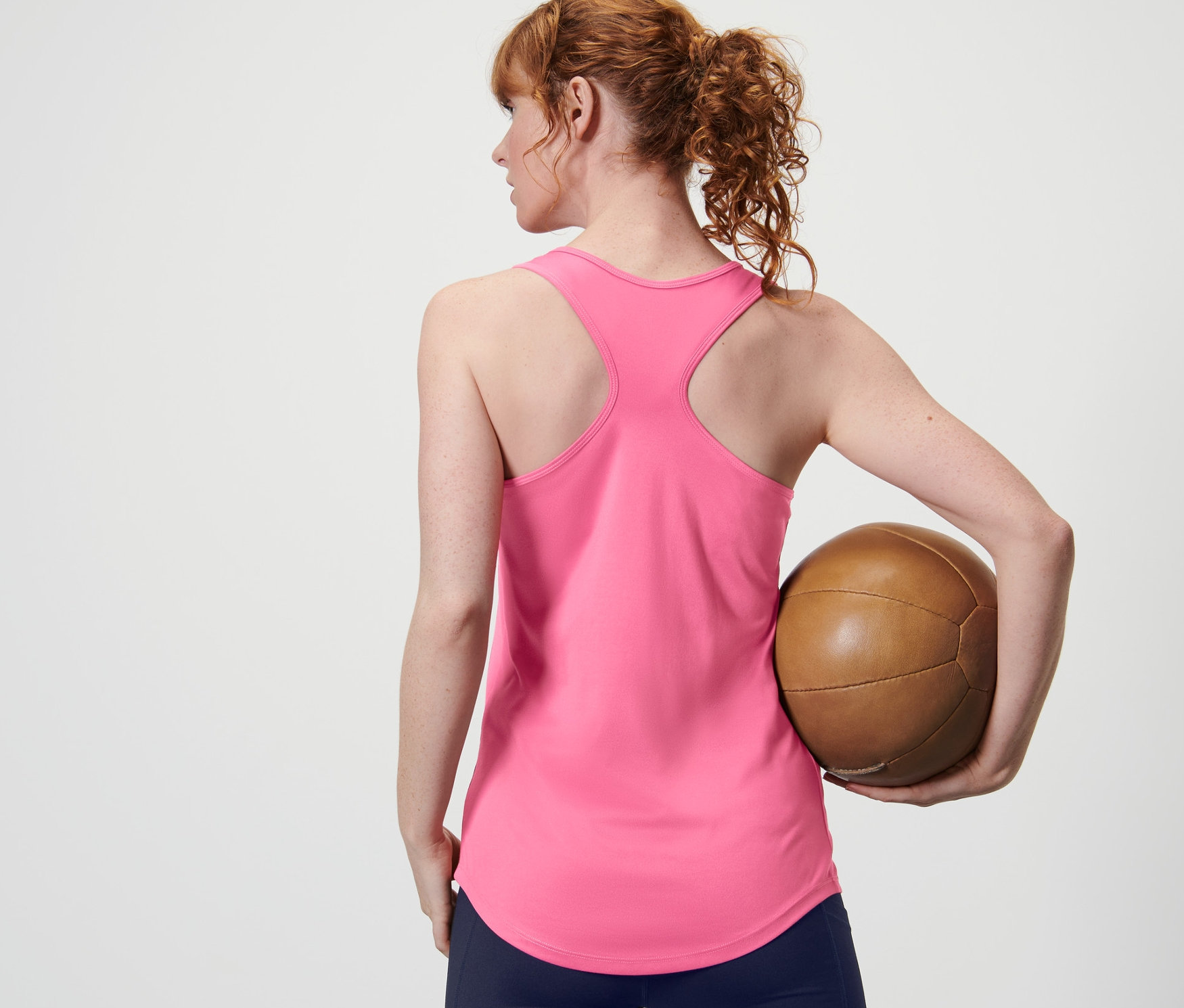 Une femme vue de dos tenant un ballon marron et portant un débardeur rose vif d'un ensemble de 2.