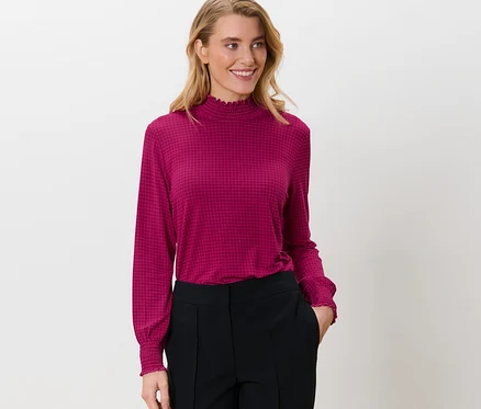 Femme portant une blouse imprimée à col montant et un pantalon noir.