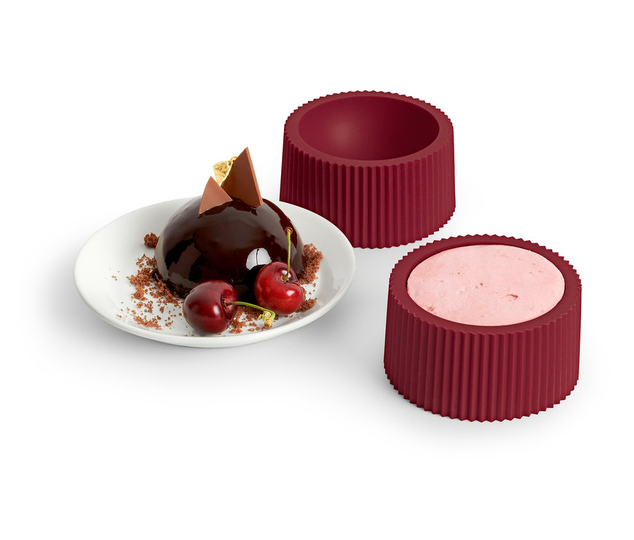 Dôme au chocolat avec cerises sur une assiette à côté de 4 moules à dessert.