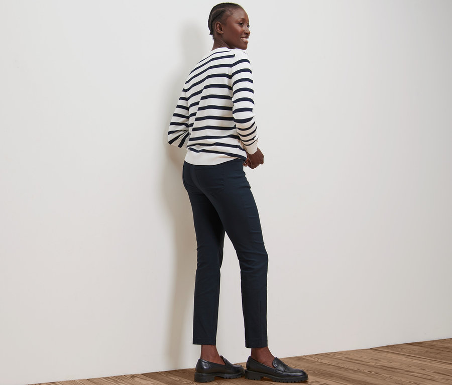 Une femme se tient de côté et porte un pantalon en bengaline bleu foncé et un pull rayé.