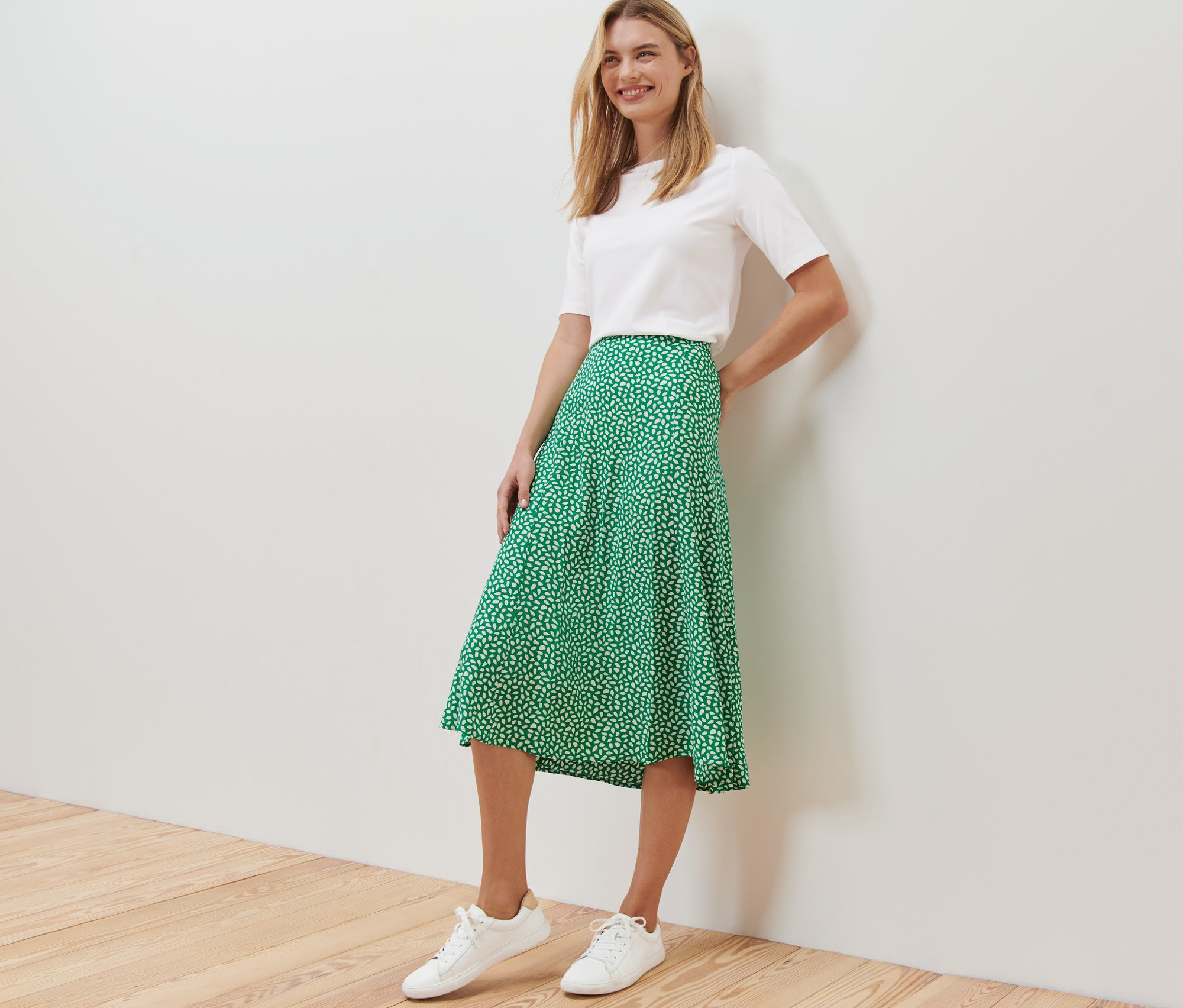 Une femme pose dans un t-shirt blanc et une jupe midi imprimée verte.