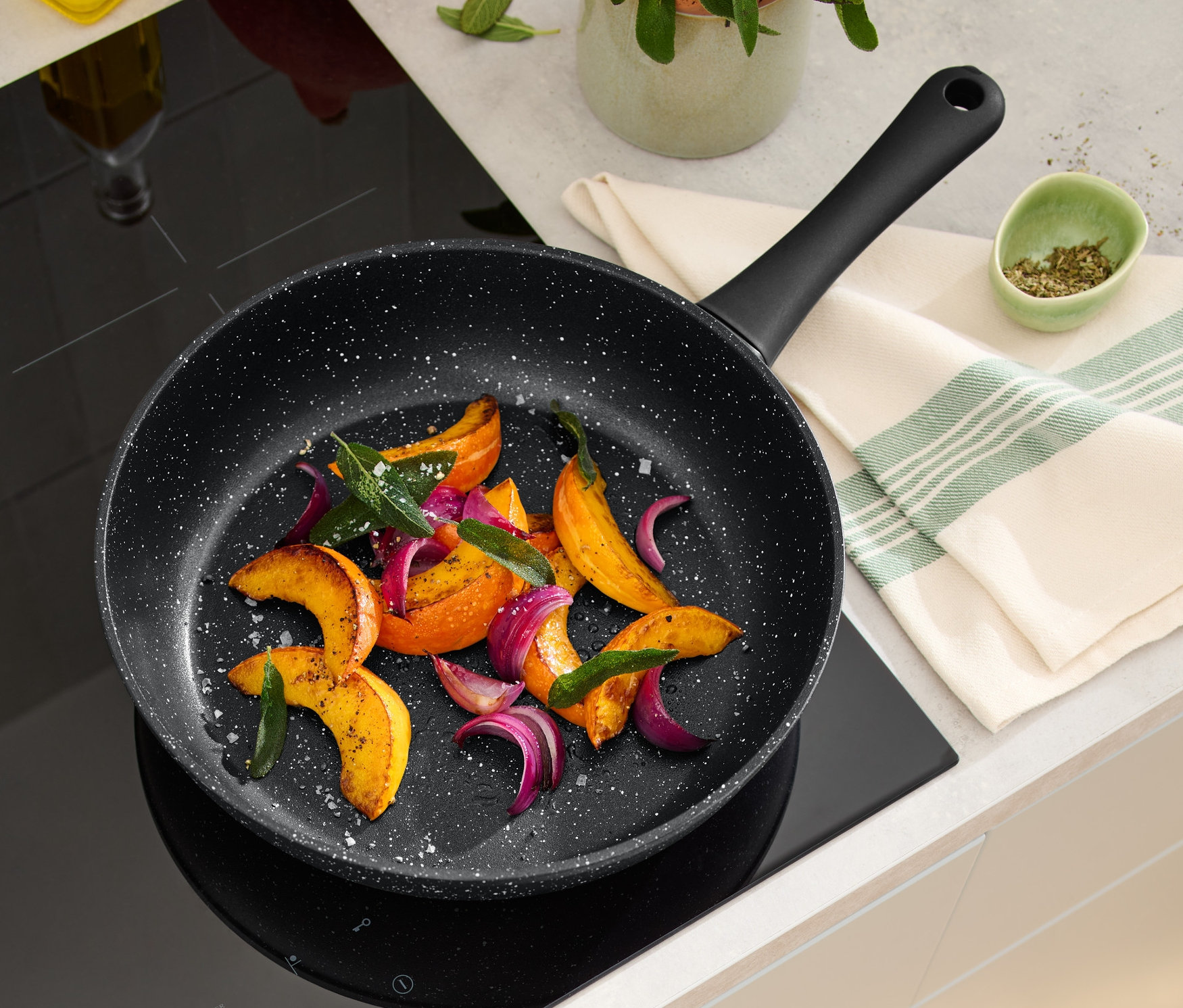 Sur une plaque à induction se trouve une poêle professionnelle aspect roche de 28 cm contenant des légumes rôtis.