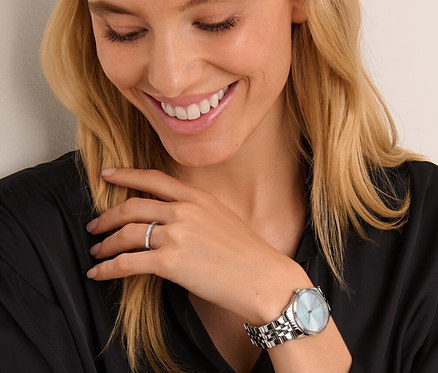 Femme souriante regardant une bague argent 925 octogone et une montre en acier inoxydable avec date.