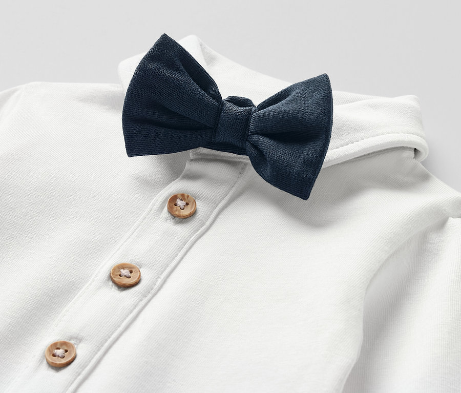 Gros plan sur un body pour bébé blanc avec nœud papillon et patte de boutonnage à boutons en bois.