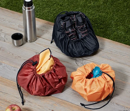 Trois fourre-tout, une thermos et une pomme sont posés sur une surface en bois.