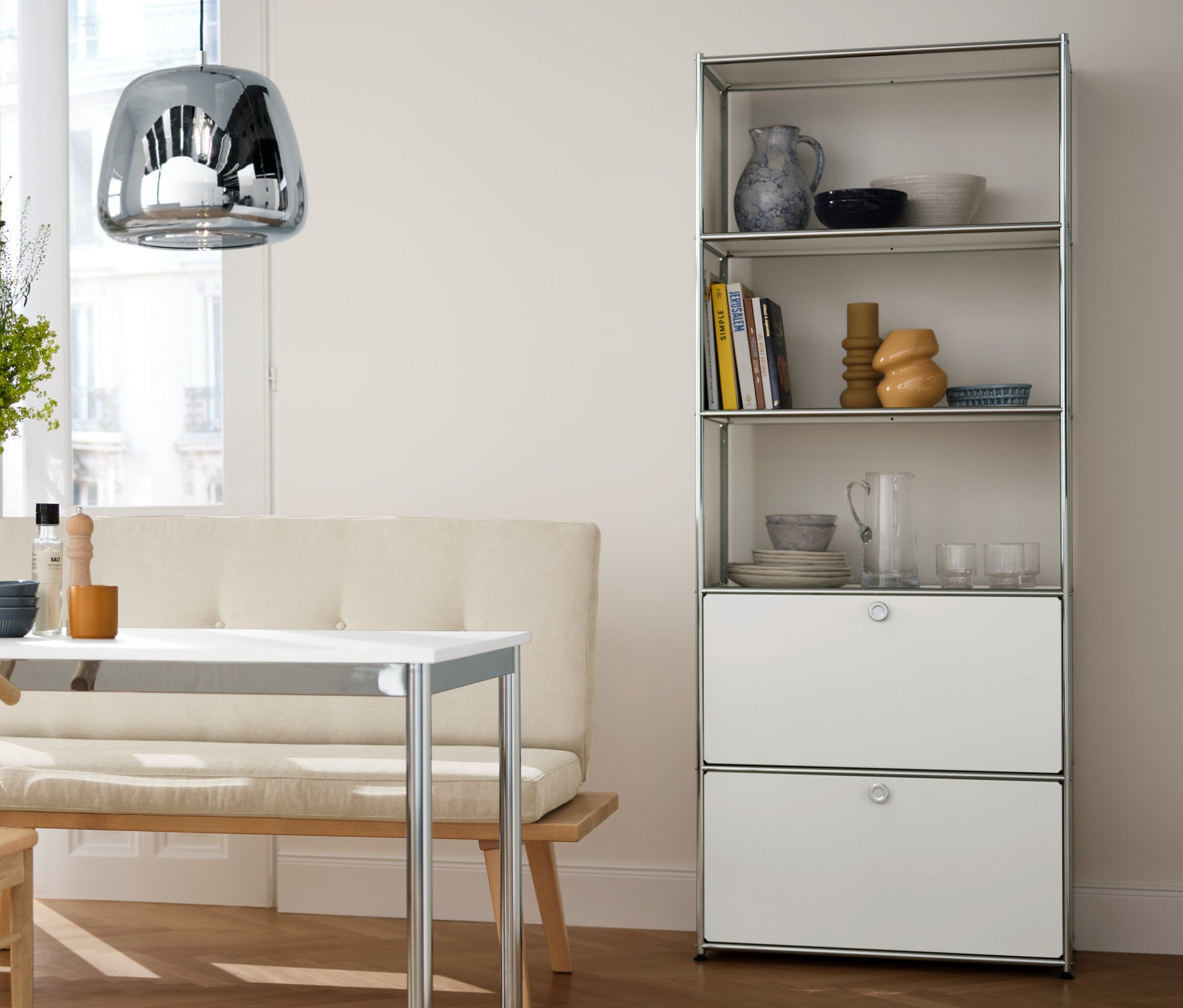 Intérieur de salle à manger avec lustre en chrome, table en métal, étagère avec tiroirs et chaises de salle à manger.