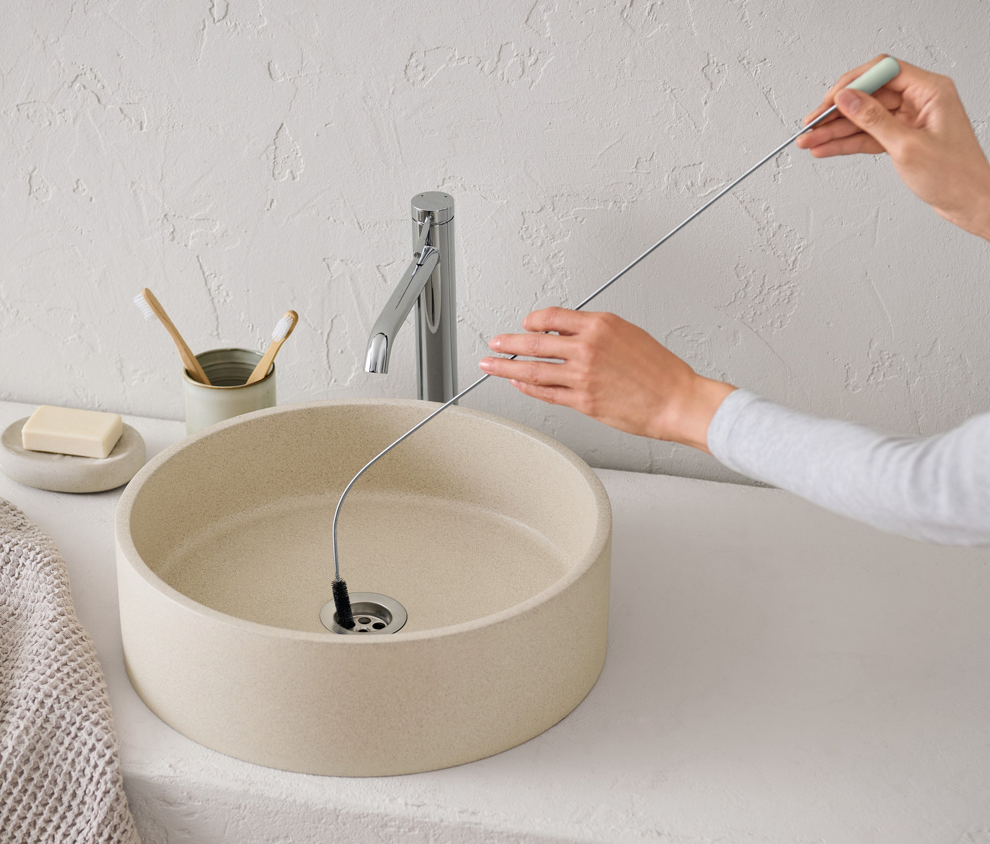 Femme nettoyant un lavabo avec une brosse d’évacuation flexible.