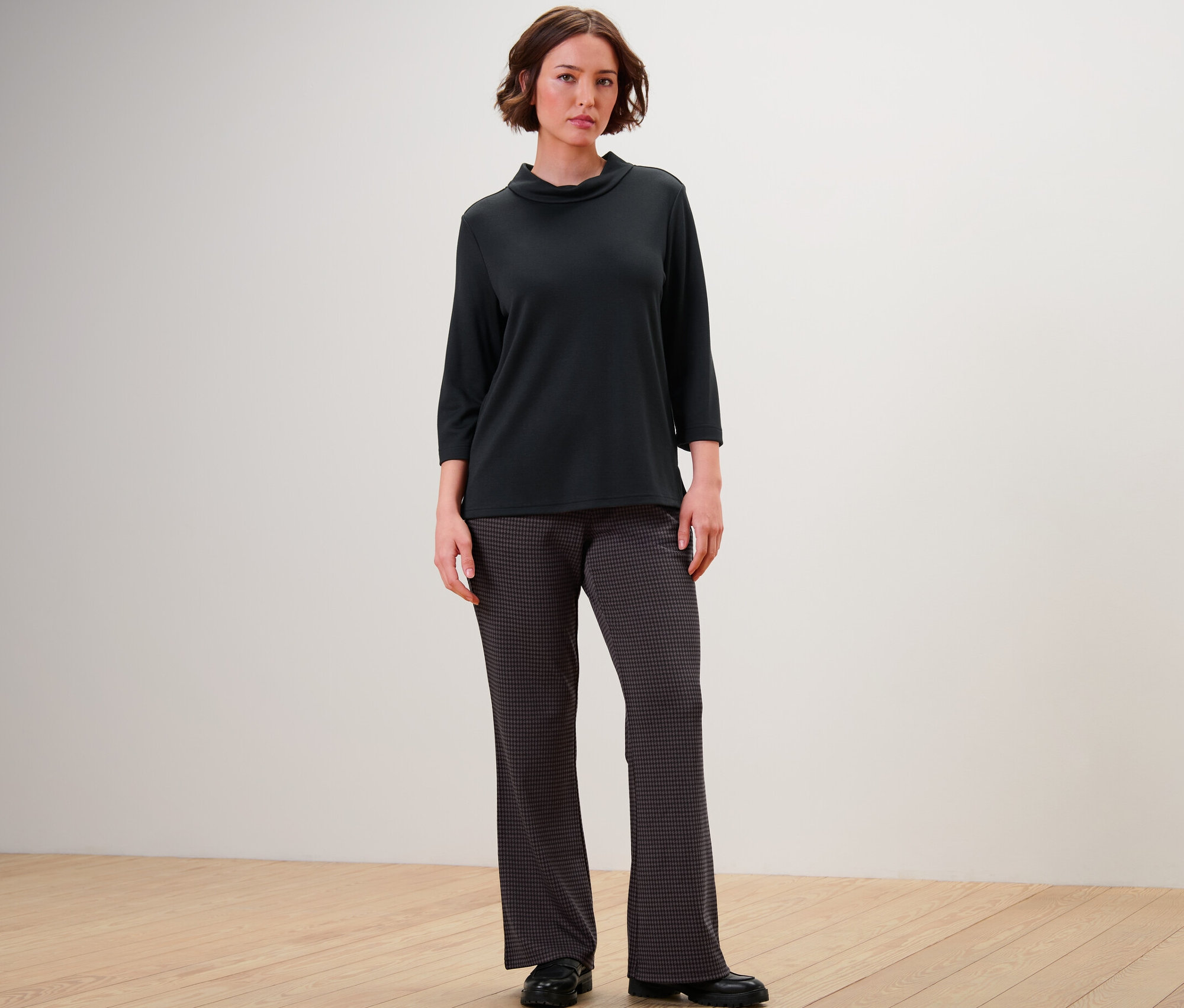 Une femme debout portant un haut noir à manches trois-quarts et un pantalon à enfiler à jacquard pied-de-poule.