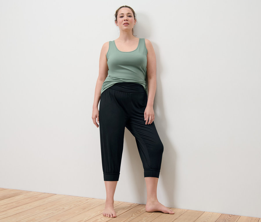 Femme posant dans un top vert et un pantalon 3/4 de yoga noir.