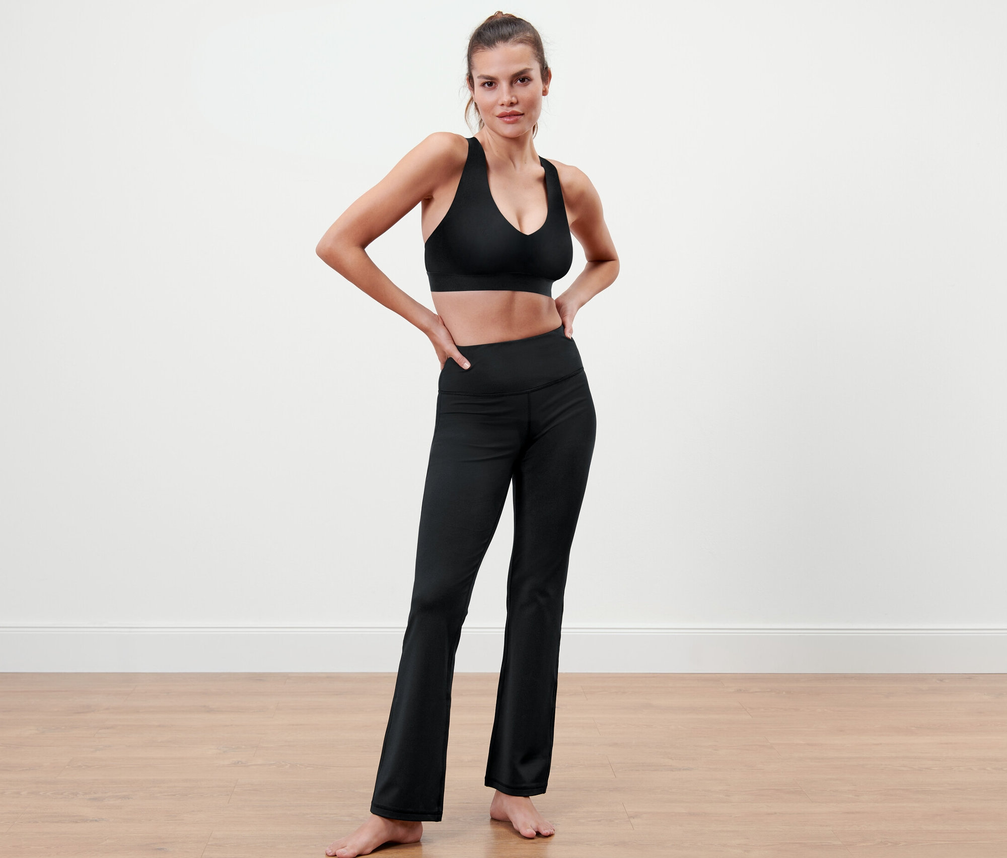 Femme posant en soutien-gorge de sport noir et pantalon de sport modelant.