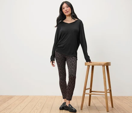Une femme se tient à côté d'un tabouret en bois et porte un haut noir à manches longues et un legging heavy imprimé.