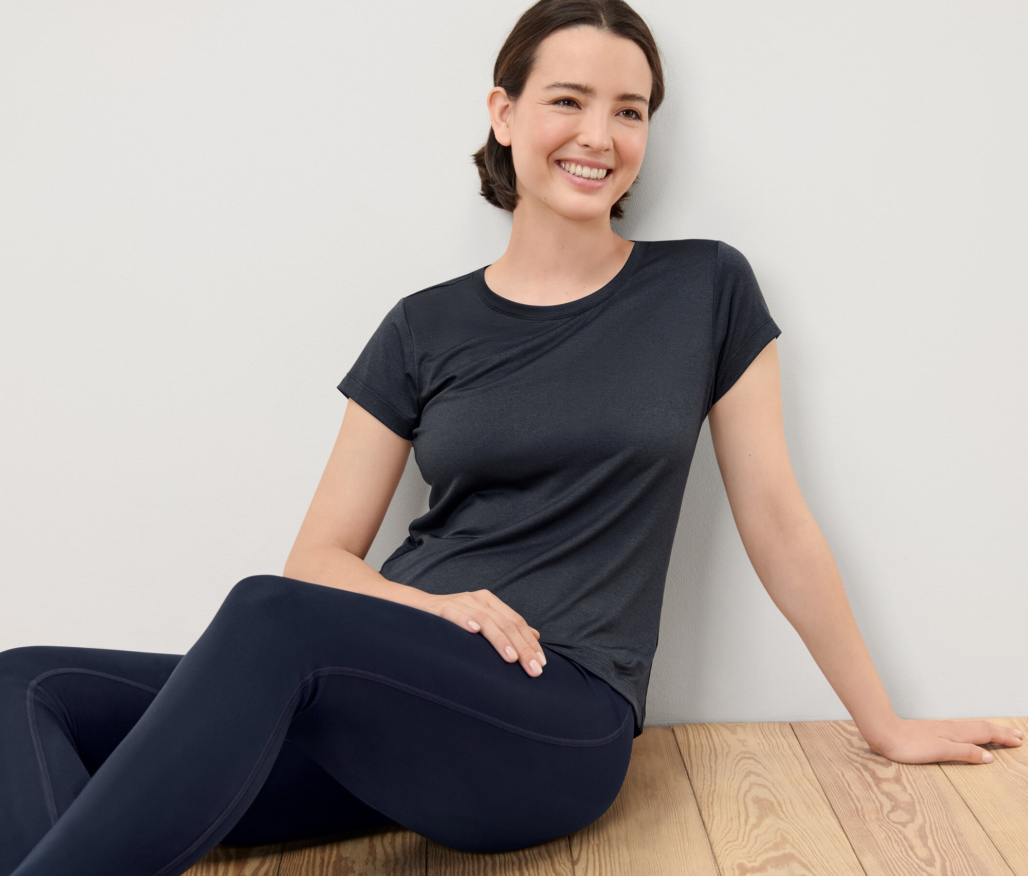 Femme assise sur un plancher en bois portant un t-shirt technique.
