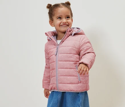 Fillette souriante portant une veste matelassée vieux rose.