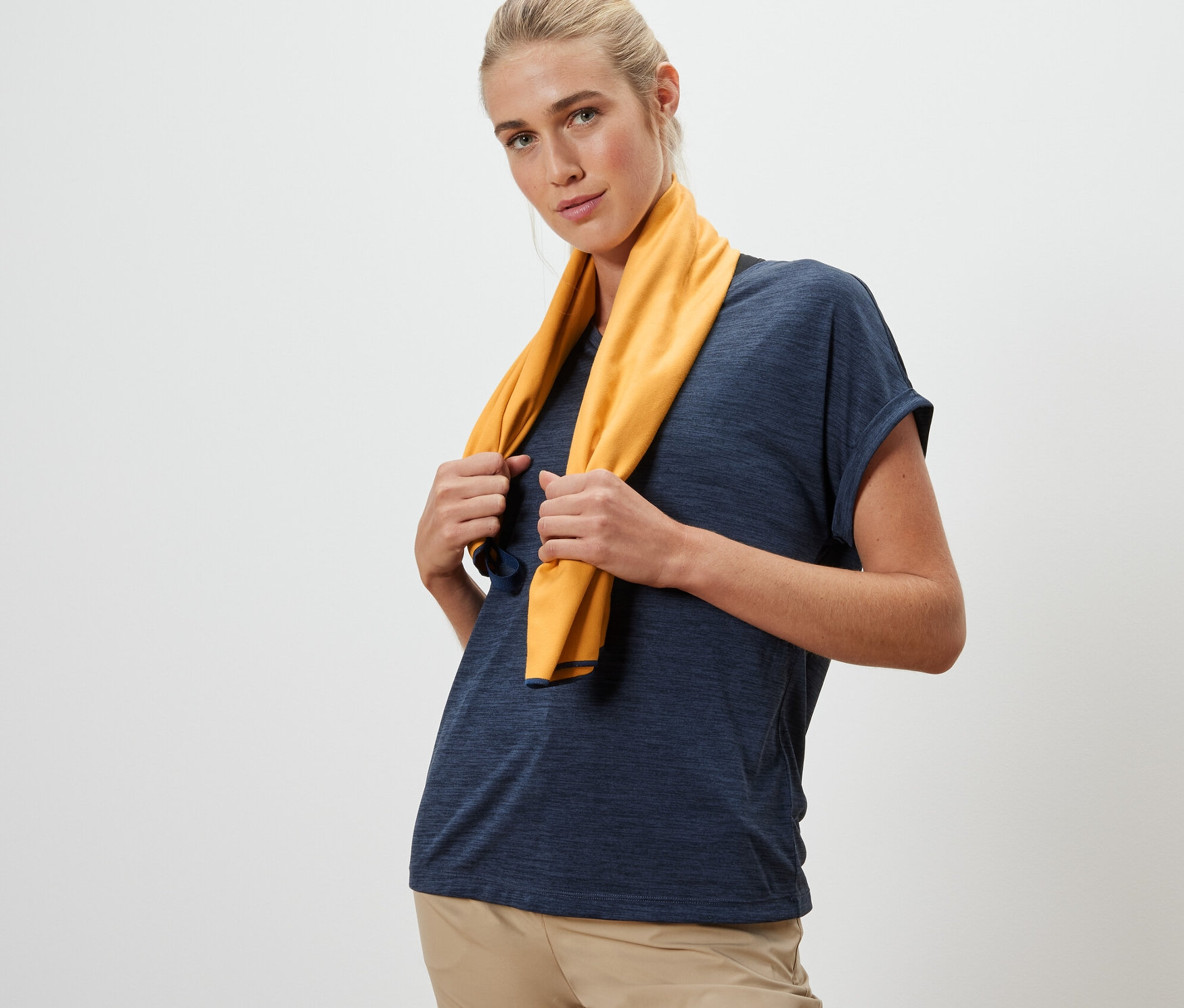 Une femme tient une serviette de toilette d’extérieur jaune d'environ 50 x 100 cm autour de son cou.