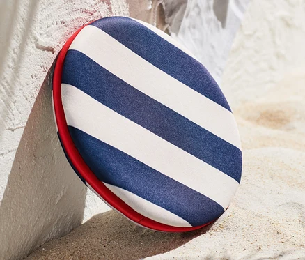 Un disque volant de sport rayé appuyé contre un mur sur le sable, avec des tongs au premier plan.
