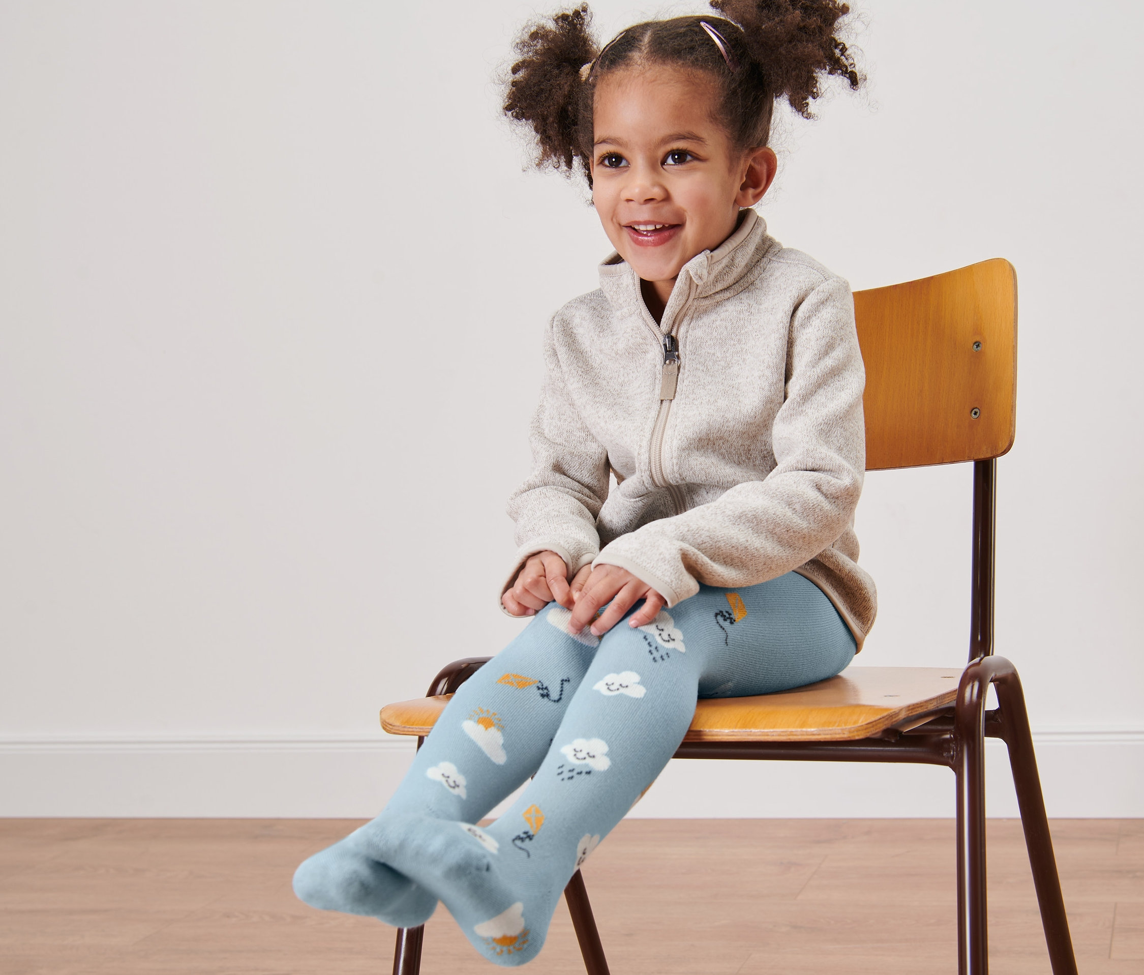 Petite fille souriante assise sur une chaise portant des collants bleus avec des nuages.