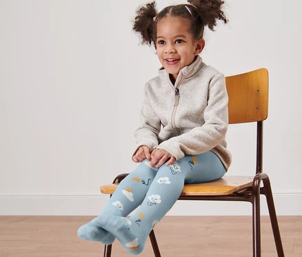 Petite fille souriante assise sur une chaise portant des collants bleus avec des nuages.