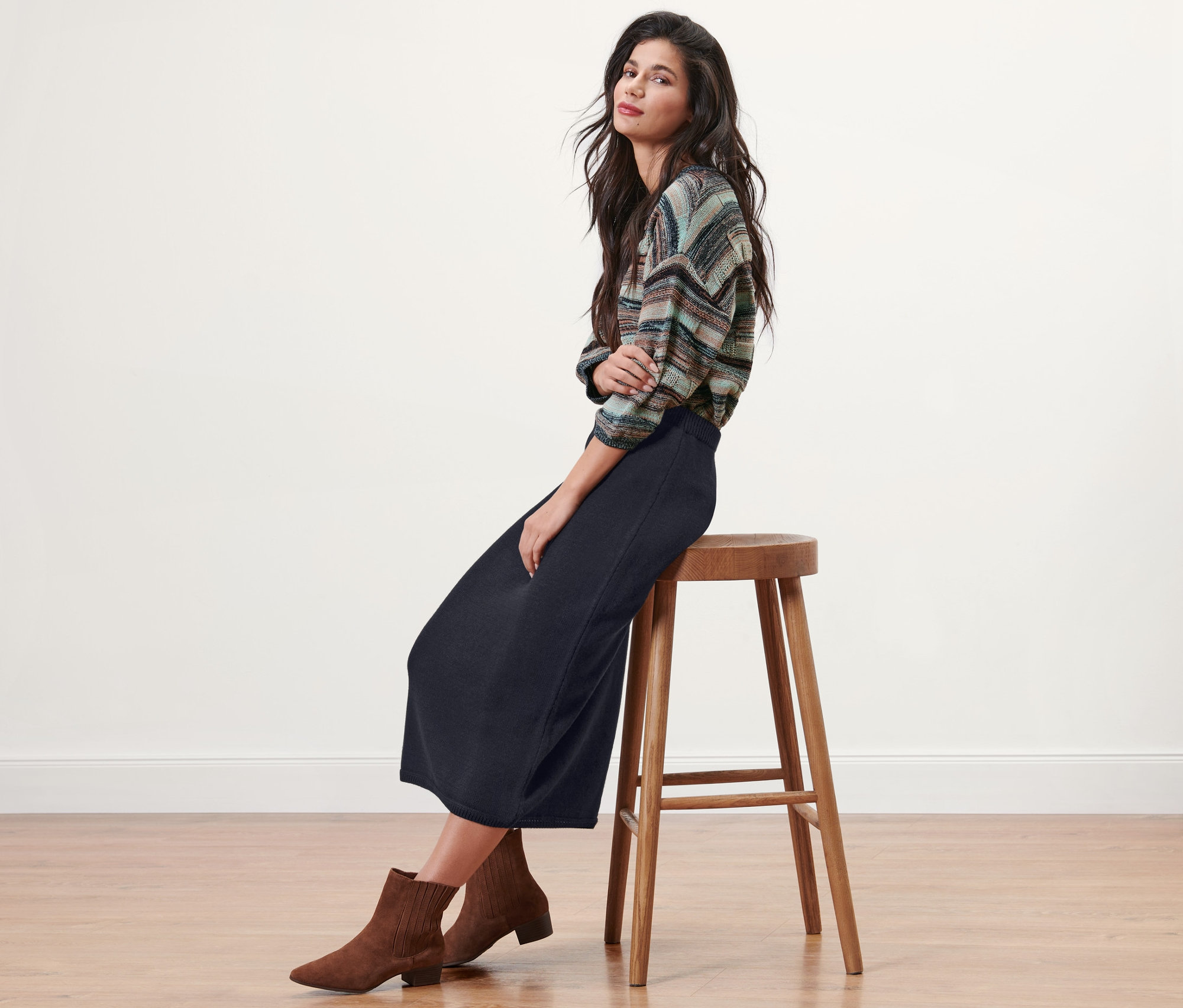 Une femme brune est assise sur un tabouret et porte une jupe tricotée bleu foncé.