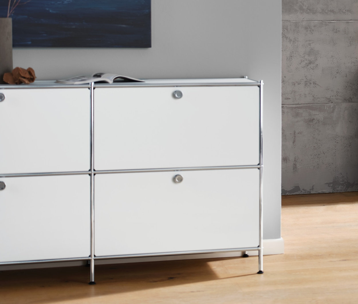 Salon avec buffet bas « CN3 » blanc avec 6 abattants, canapé 3 places anthracite, lampe de table blanche avec abat-jour en tissu et table basse à roulettes « CN3 » blanche.