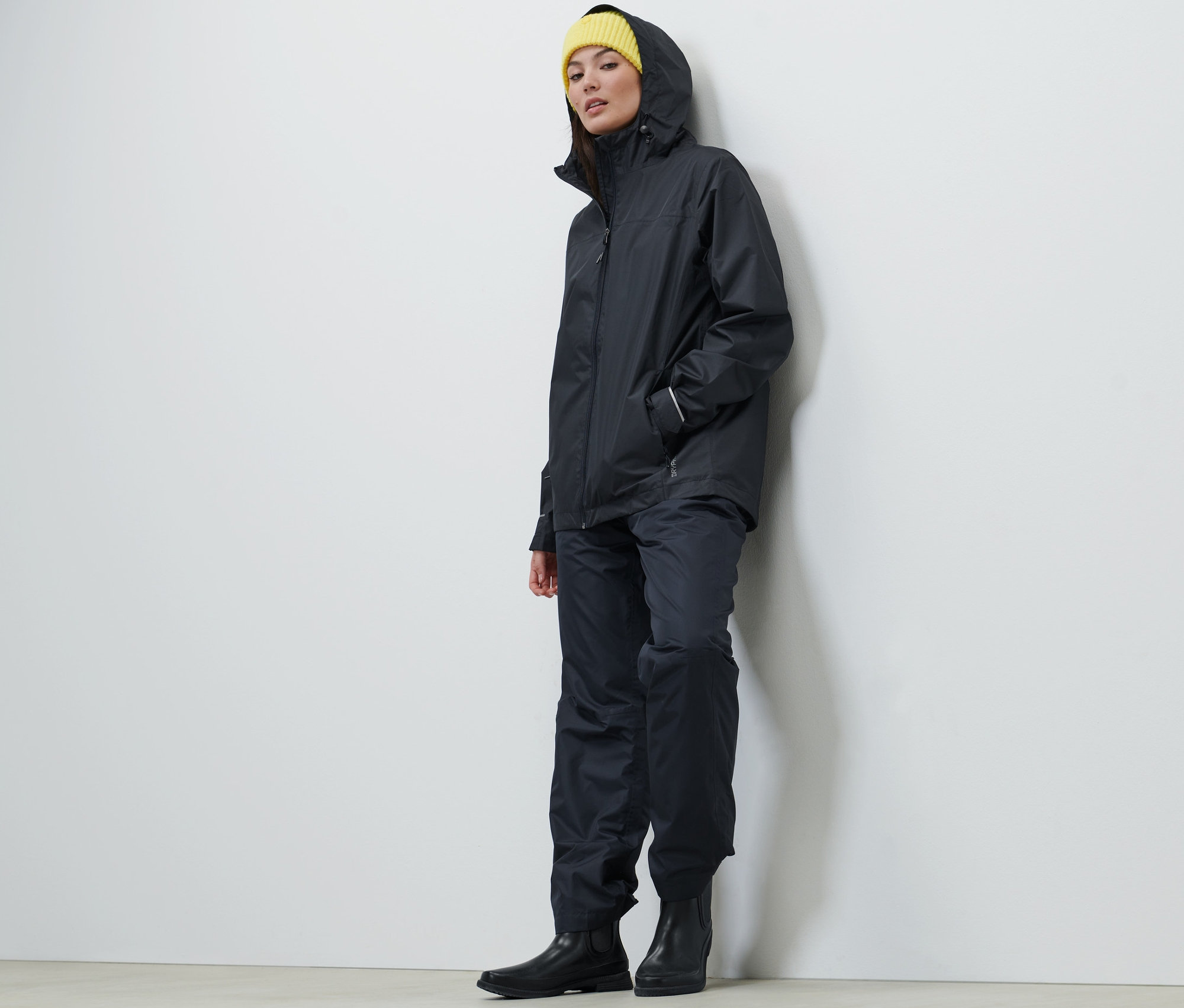 Une femme portant une veste de pluie unisexe bleu foncé, un pantalon et un bonnet jaune.