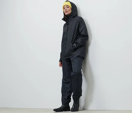 Une femme portant une veste de pluie unisexe bleu foncé, un pantalon et un bonnet jaune.