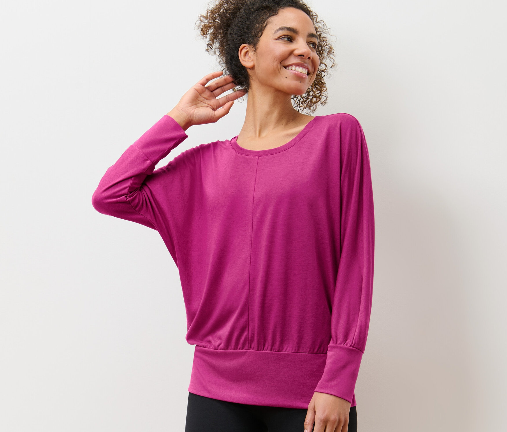 Femme posant en T-shirt de yoga devant un mur blanc.