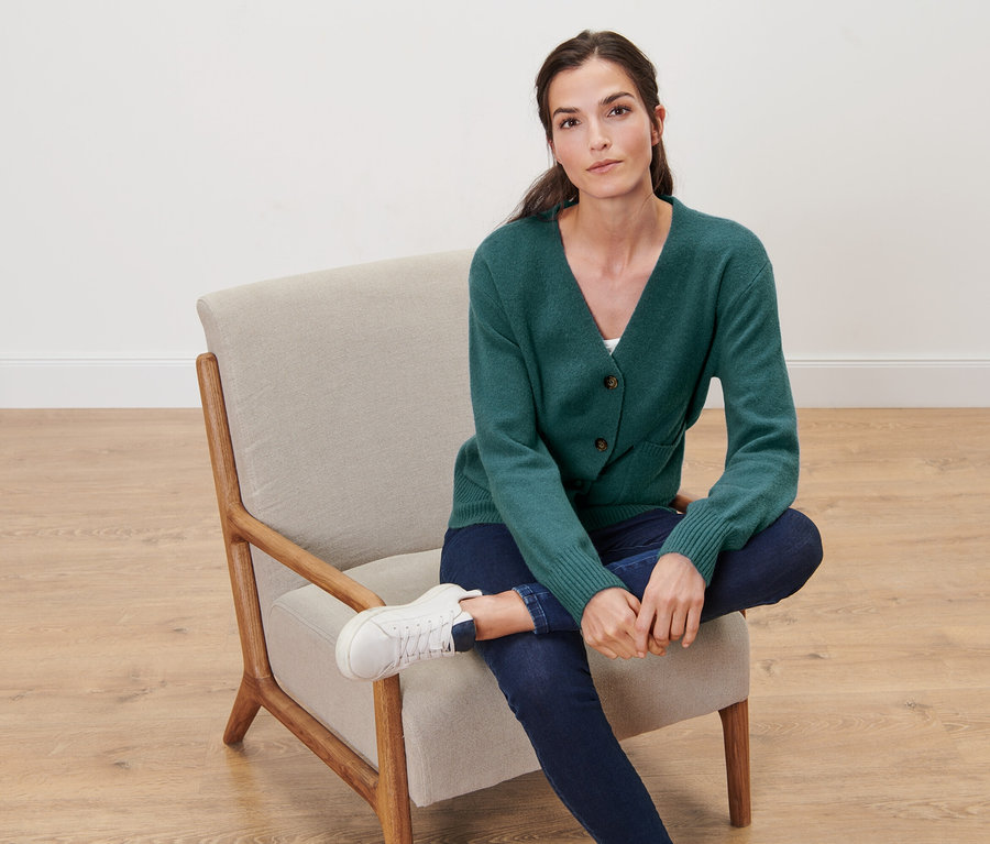 Femme assise dans un fauteuil portant une jaquette en maille avec de la laine, vert foncé.