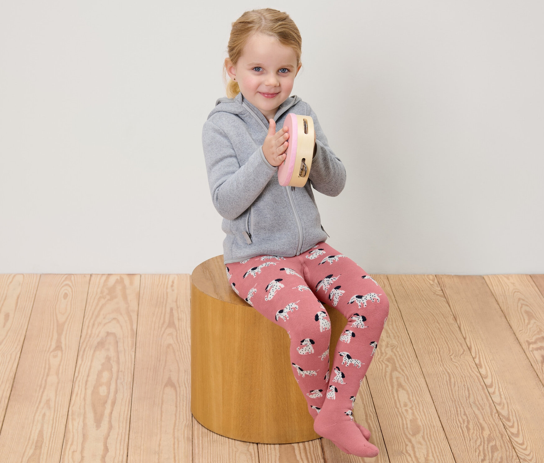 Une fille assise joue du tambourin et porte des collants thermiques roses et gris pour enfants.