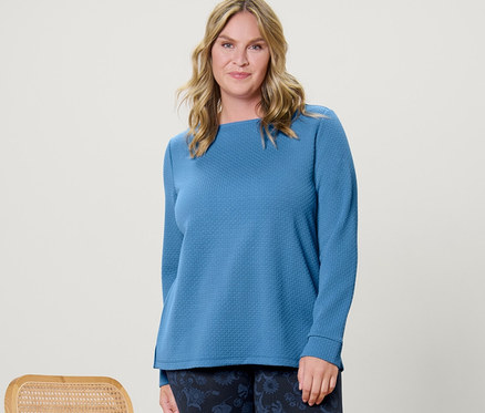 Une femme pose à côté d'une chaise, portant un sweat-shirt structuré et un legging imprimé.