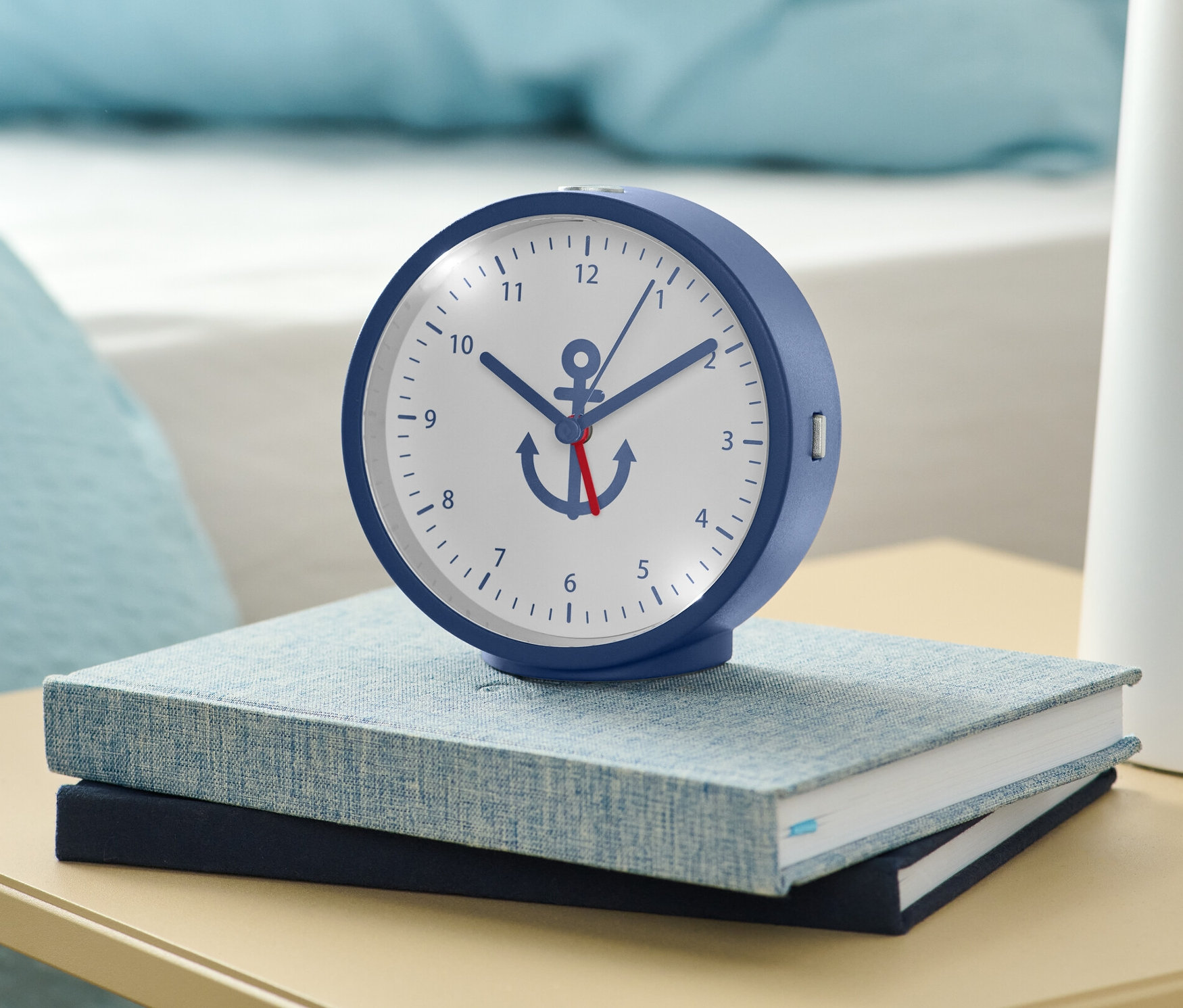 Un réveil bleu avec rétro-éclairage posé sur deux livres sur une table de chevet.