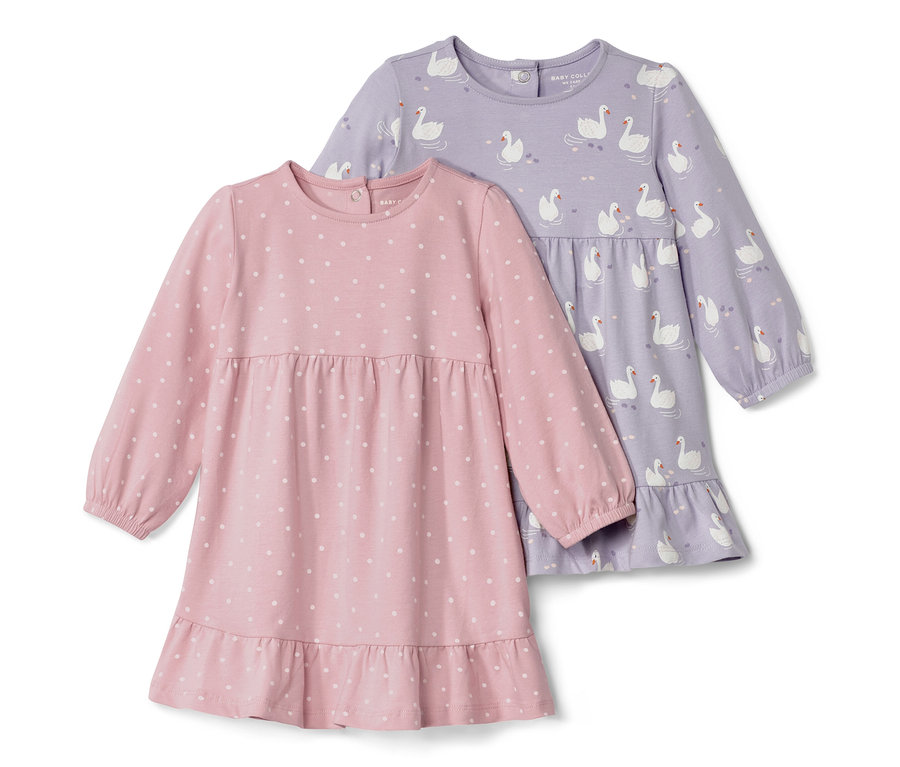 Deux robes en jersey pour bébé : une rose à pois blancs, l’autre violette avec un motif de cygnes.