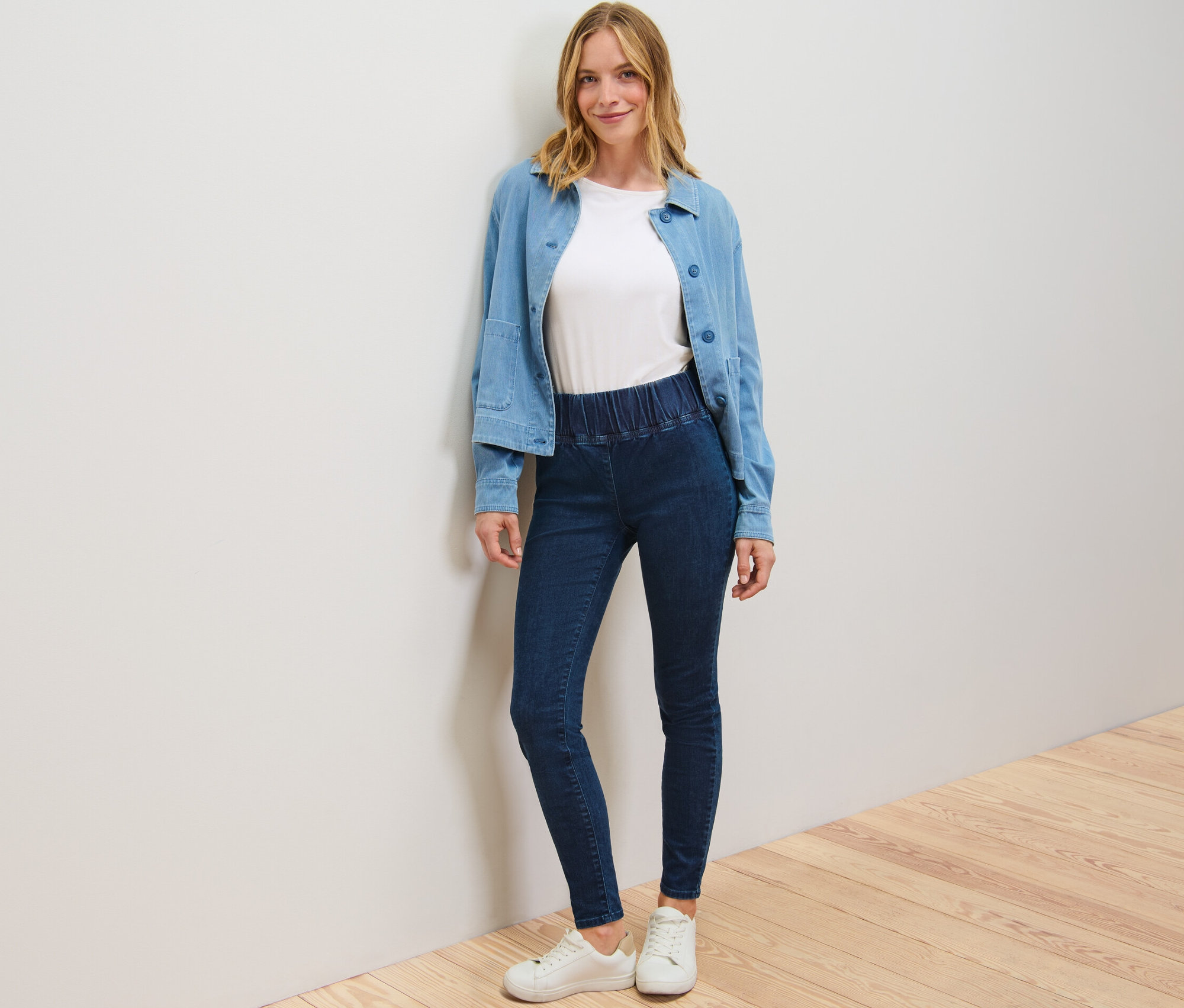 Femme posant en legging taille haute en denim, t-shirt blanc et veste bleue.
