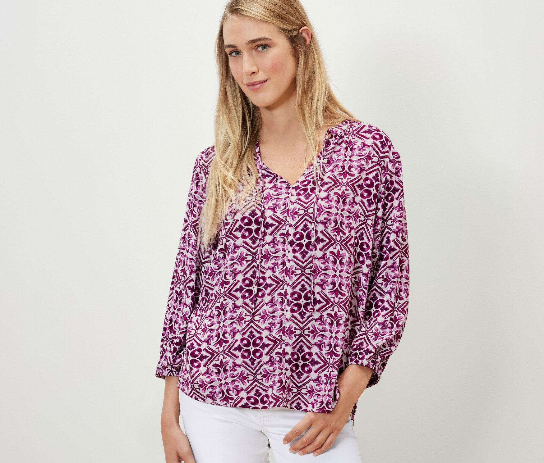 Femme portant un chemisier-tunique imprimé, baies et un jean blanc.