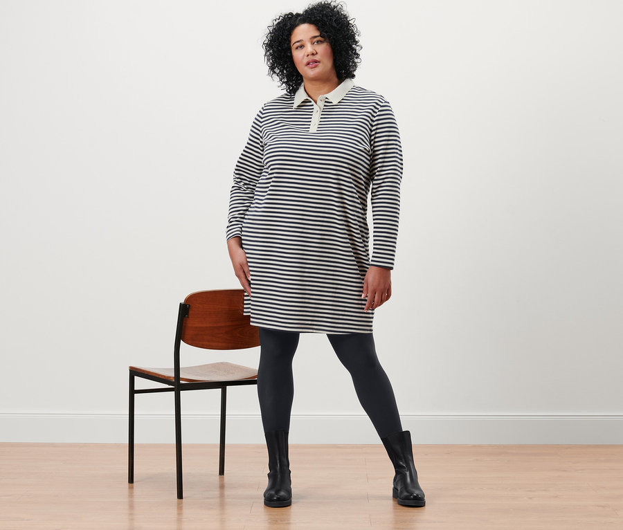 Une femme pose en robe molletonnée à rayures avec col polo et 2 paires de collants opaques noirs.