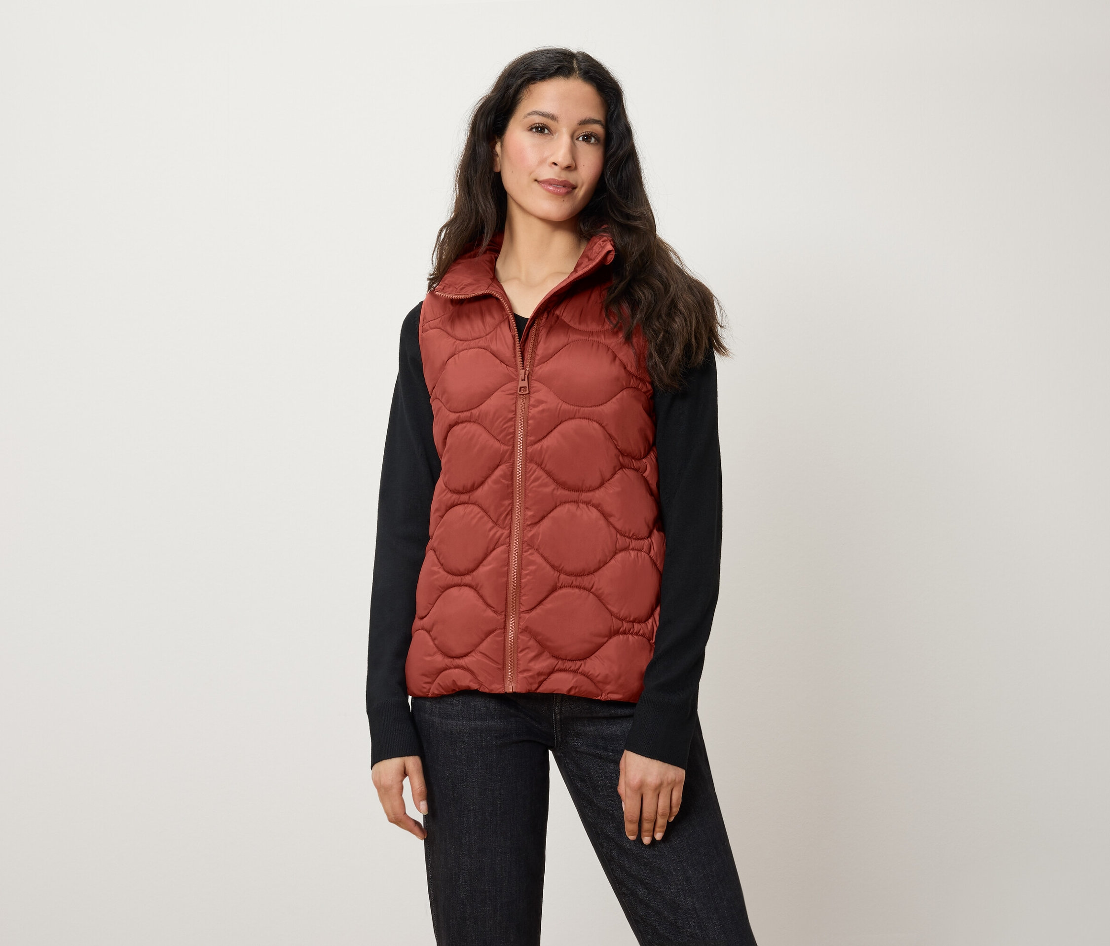 Une femme porte un gilet matelassé couleur rouille.
