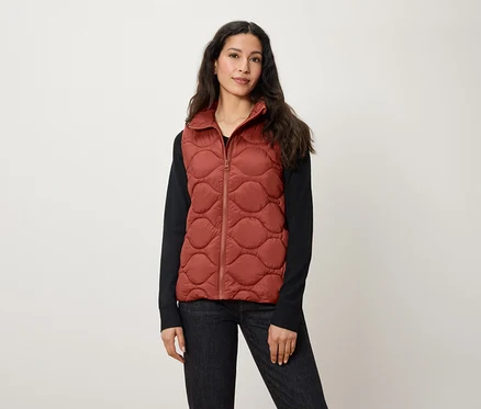 Une femme porte un gilet matelassé couleur rouille.
