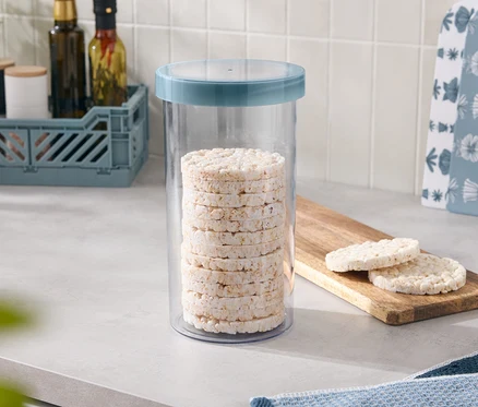 Des galettes de riz sont empilées dans un récipient avec un couvercle bleu, deux autres sont posées sur une planche en bois.