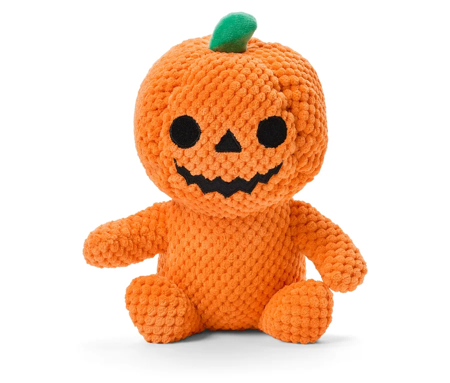 Une peluche citrouille orange avec une tige verte, des yeux noirs et un sourire assise sur un fond blanc.