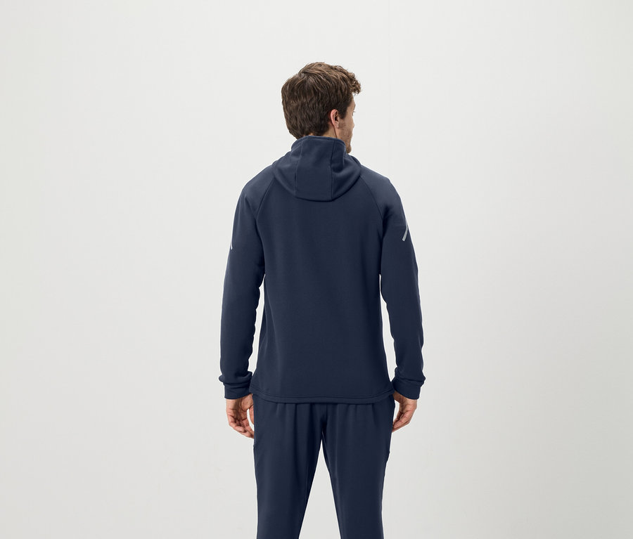 Un homme vu de dos porte un sweat à capuche bleu marine et un pantalon de survêtement.