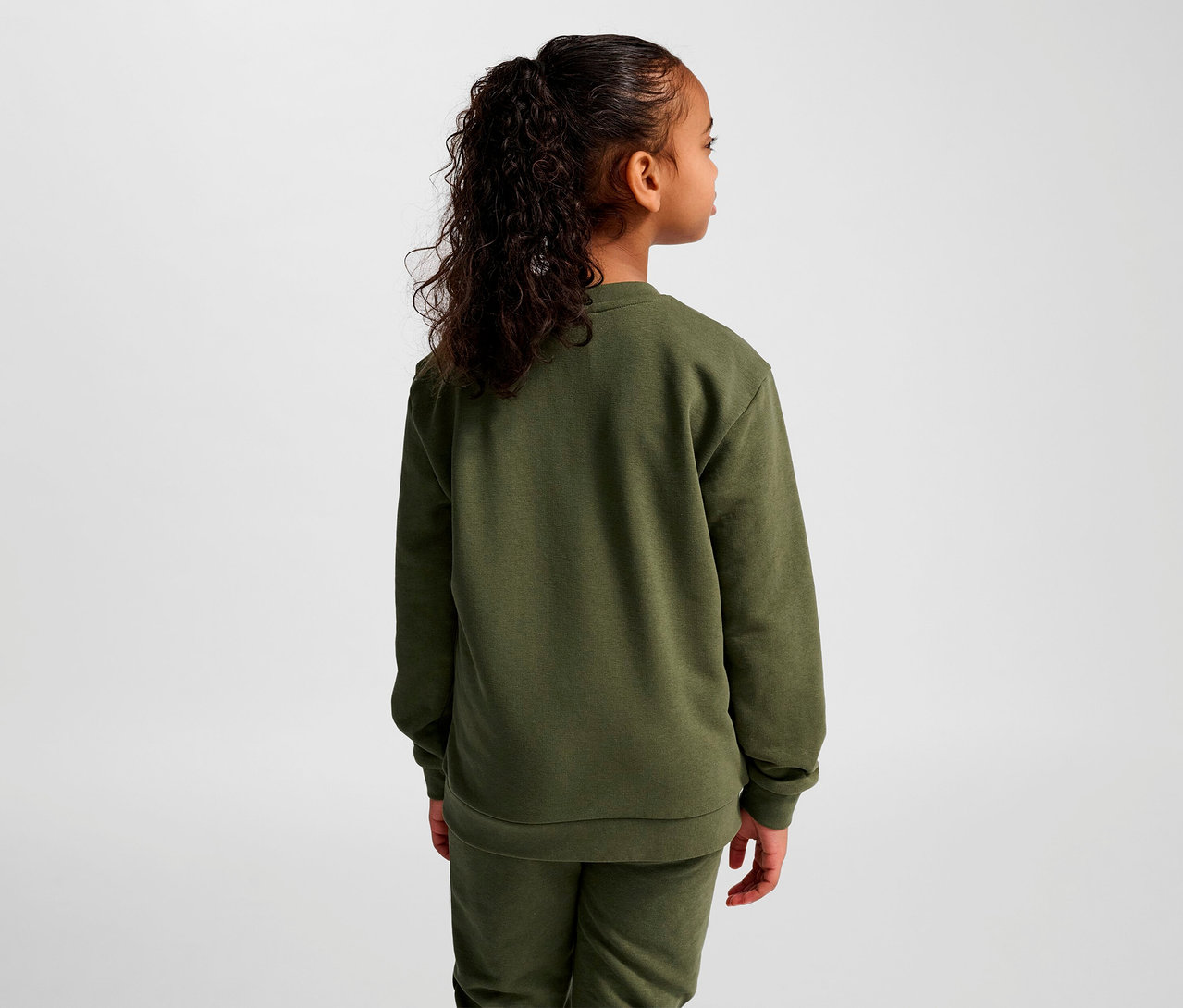 Une fille, vue de dos, porte un sweat-shirt HUMMEL HMLJR Base vert.